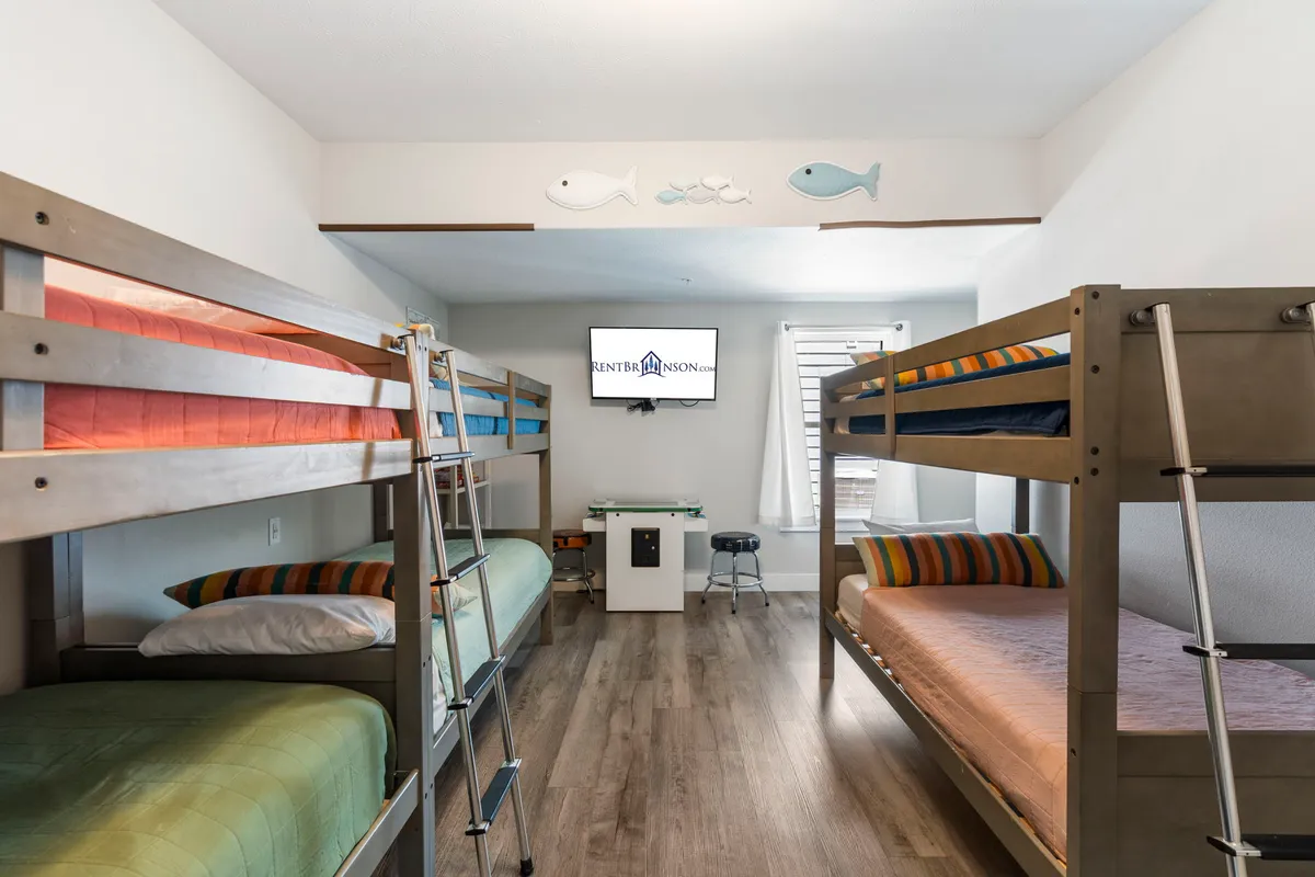 A cheerful kid-friendly bunk room with triple bunk beds, colorful bedding, a television, and plenty of space to play or watch TV. The decor is playful and the atmosphere is welcoming, making it an ideal retreat for children to create memories together.