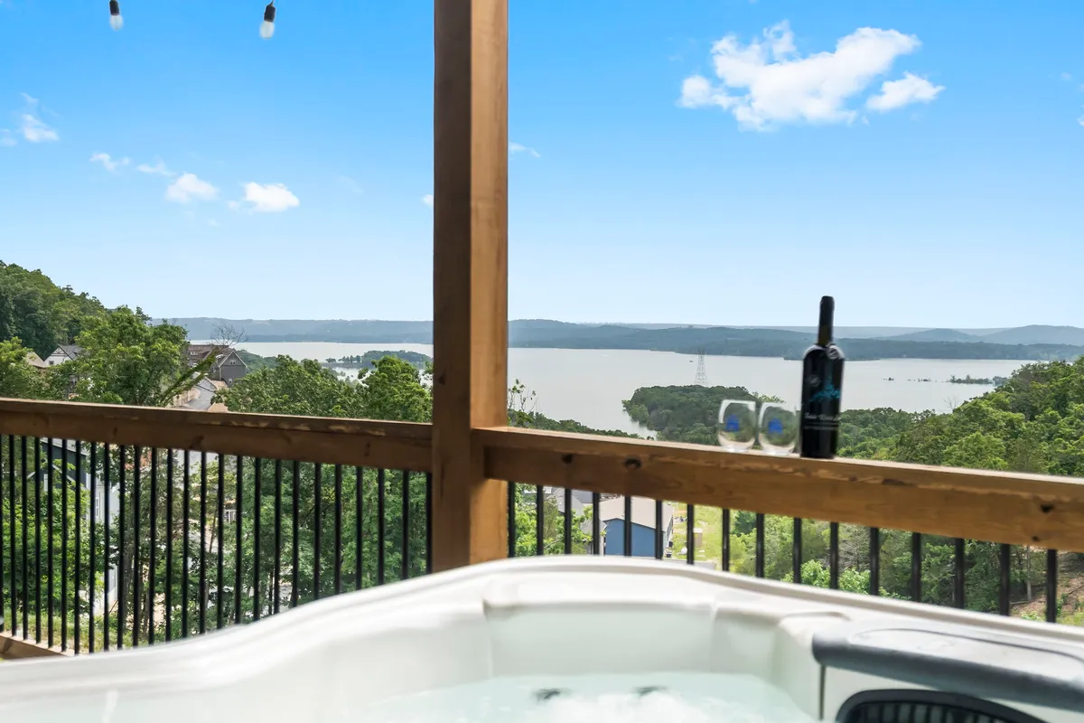 An inviting exterior scene with a private hot tub overlooking a scenic lake view. A bottle of wine and glasses are set up for a relaxing soak under the stars, with tranquility and comfort at the forefront.