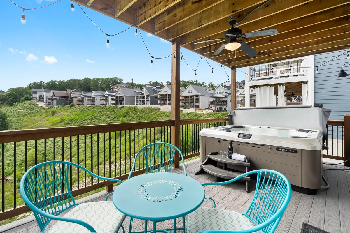 A relaxing outdoor deck featuring a bubbling hot tub, comfortable seating area, and views of neighboring upscale homes. The setting is perfect for unwinding after a day of adventure, inviting guests to soak in the tub while enjoying the sunset or night sky.