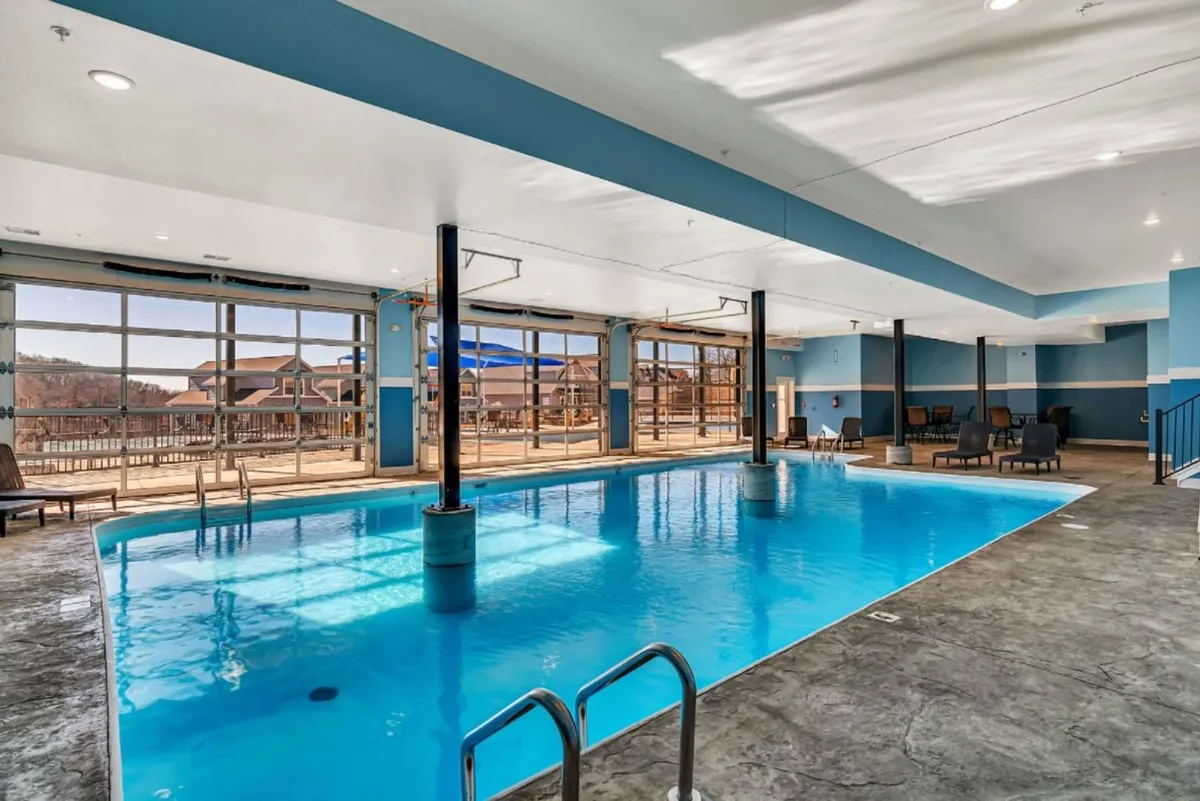 This interior image features a serene indoor swimming pool with large windows that let in natural light, complemented by lounge chairs along the poolside. The setting is calm and inviting, perfect for year-round swimming and relaxation.