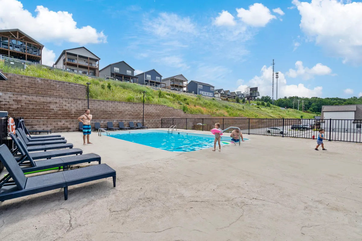 An exterior view of the outdoor swimming pool area, where children play in the water and families gather on lounge chairs. The mood is bright and cheerful, emphasizing active fun and togetherness under the sun.