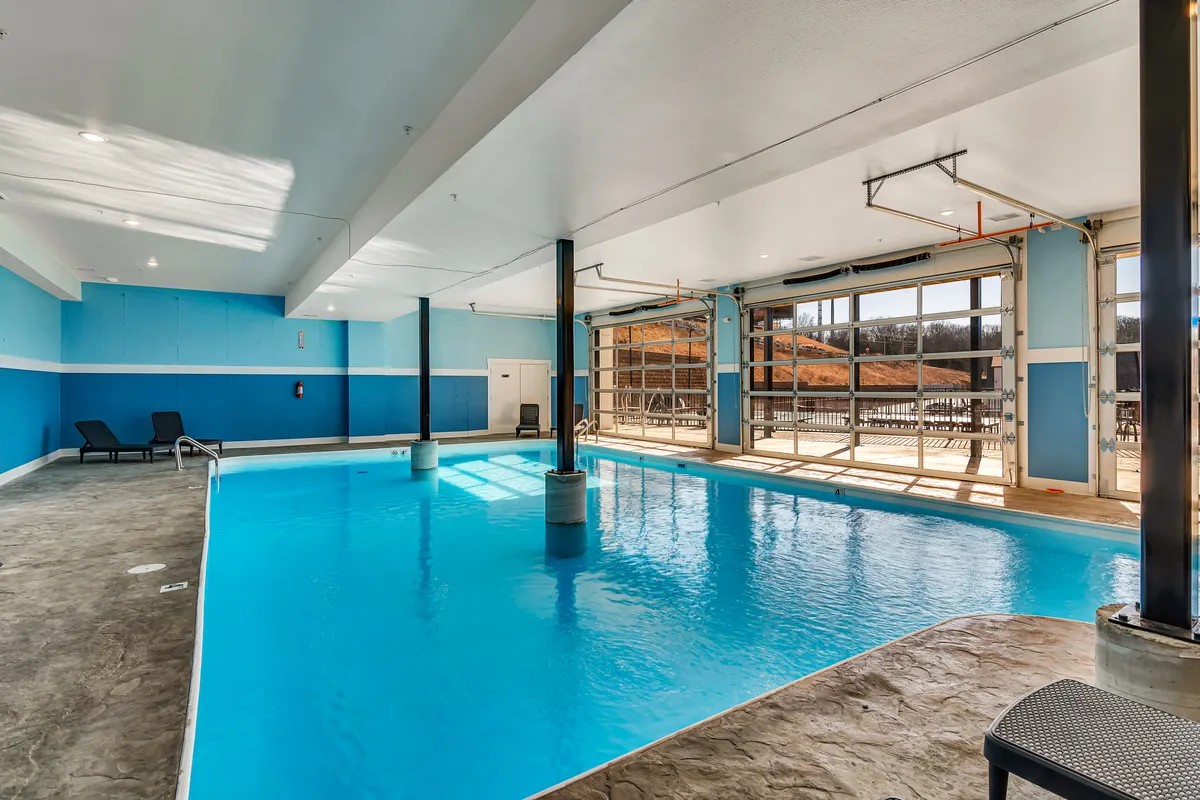 This interior image showcases a large indoor swimming pool area with lounge chairs and a wide garage door that hints at indoor-outdoor flexibility. Natural light streams in, and the atmosphere is tranquil yet inviting, perfect for year-round swimming and relaxing with family or friends.