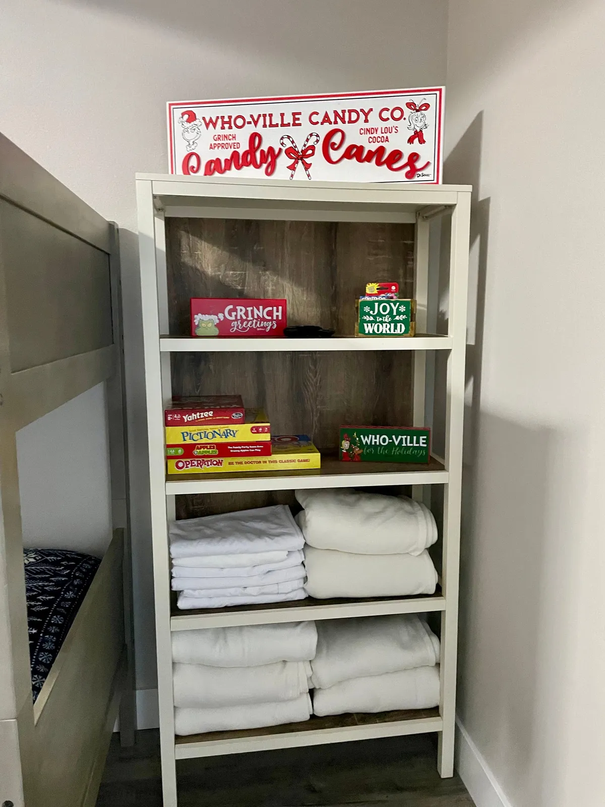 A playful game area highlighted by a vibrant 'Who-Ville Candy Co.' sign, a neat stack of board games, and folded towels. The design evokes a cheerful, family-friendly environment perfect for tournaments and fun nights in.